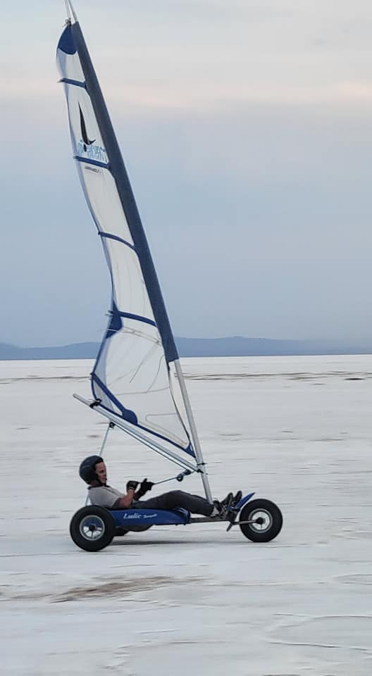 Un pilote de char à voile manœuvre habilement son véhicule à travers une étendue salée sous un ciel calme et nuageux, propulsé par le vent dans une aventure écologique au cœur de Djibouti.