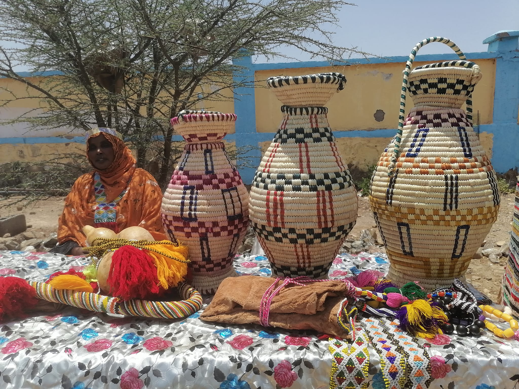 Artisane locale à Dasbiyo présentant des paniers traditionnels et des bijoux faits main, en arrière-plan un paysage typique de la région d'Ali Sabieh.